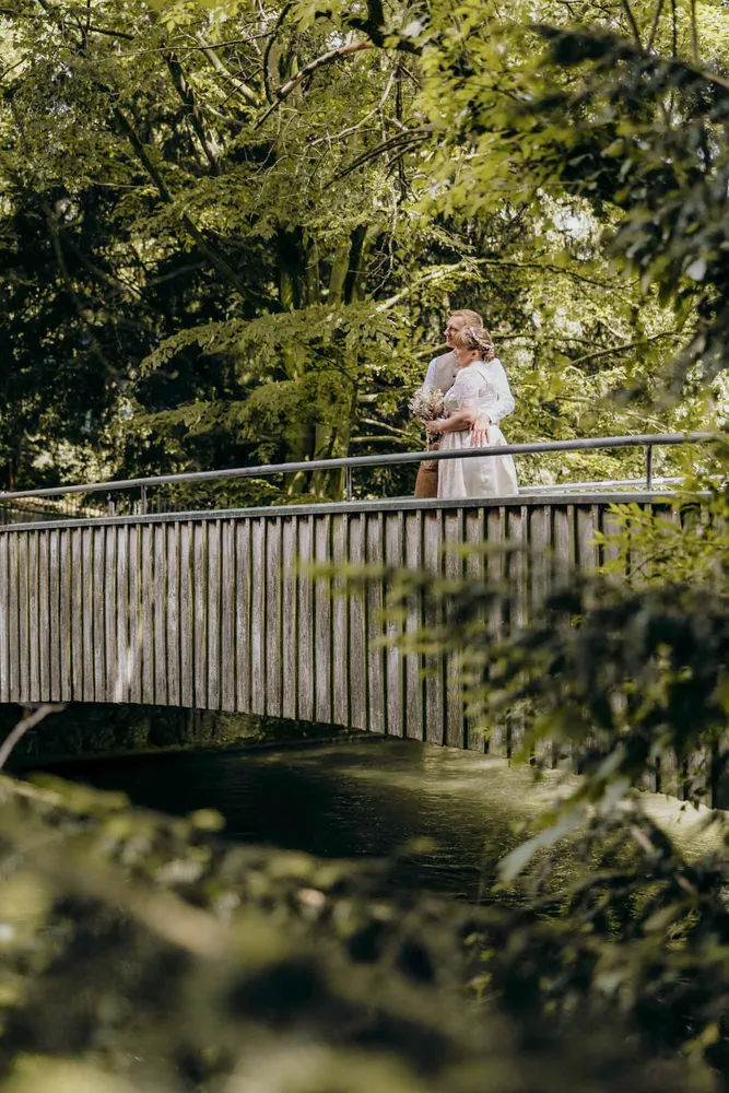 Paar steht lächelnd auf einer Brücke über einem Fluss