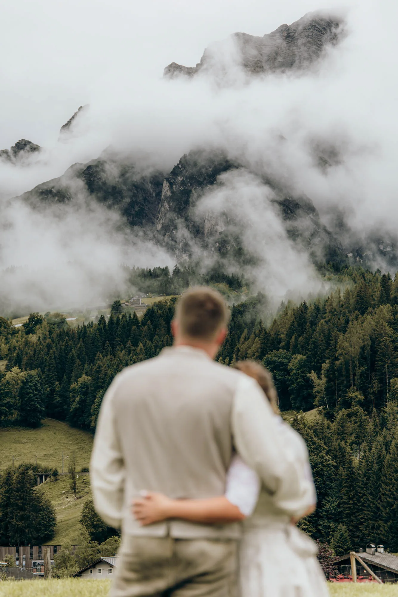 Paar von hinten, Arm in Arm, blickt auf bewölkte Berge